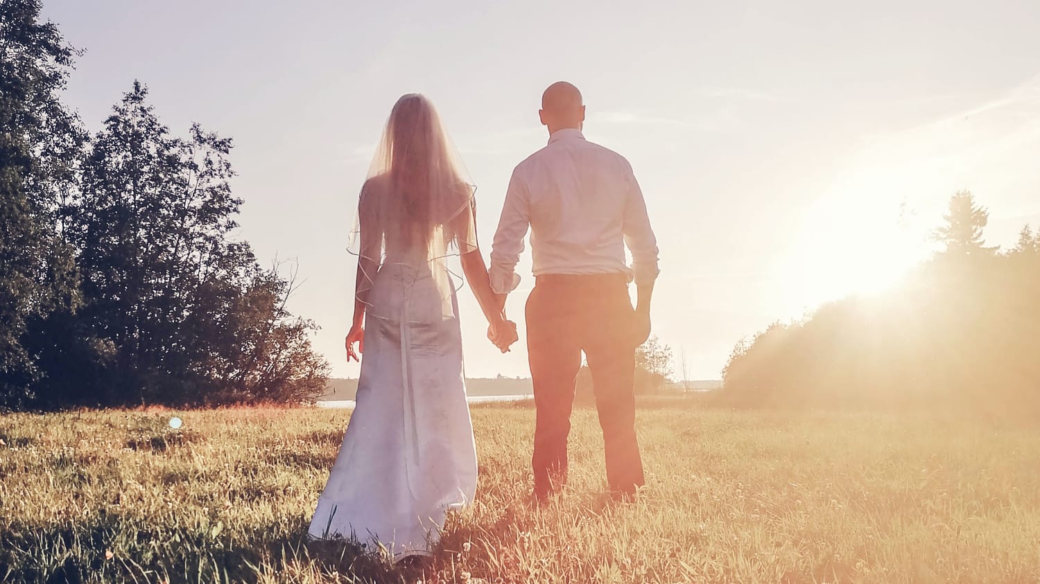 Newly married couple holding hands in a field in Raahe in sunset.
