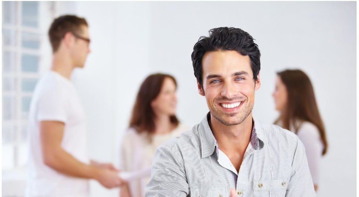 Smiling professional in an office while colleagues talk in the background