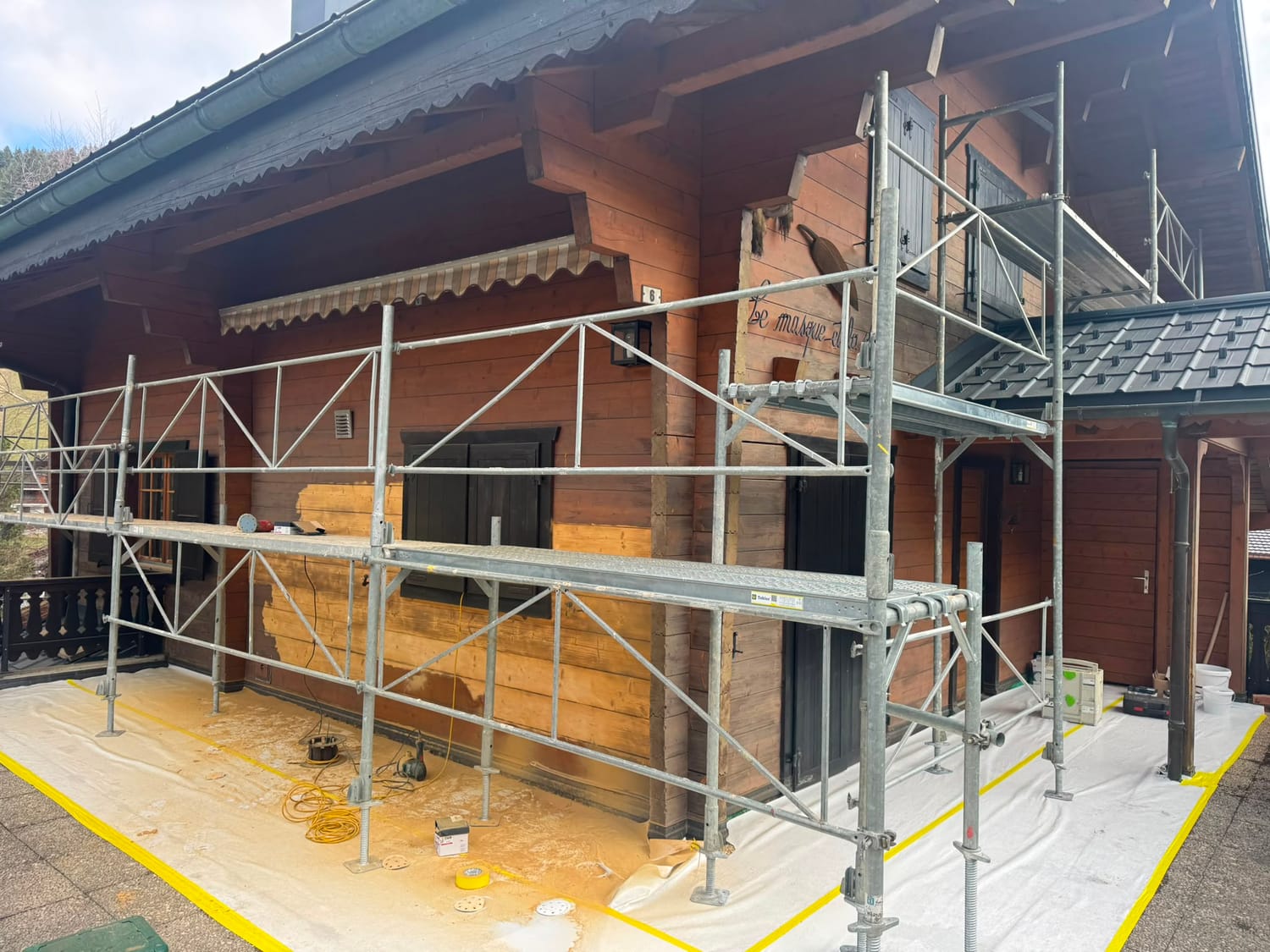 Façade en bois en cours de lasure, bois brut et teinté côte à côte