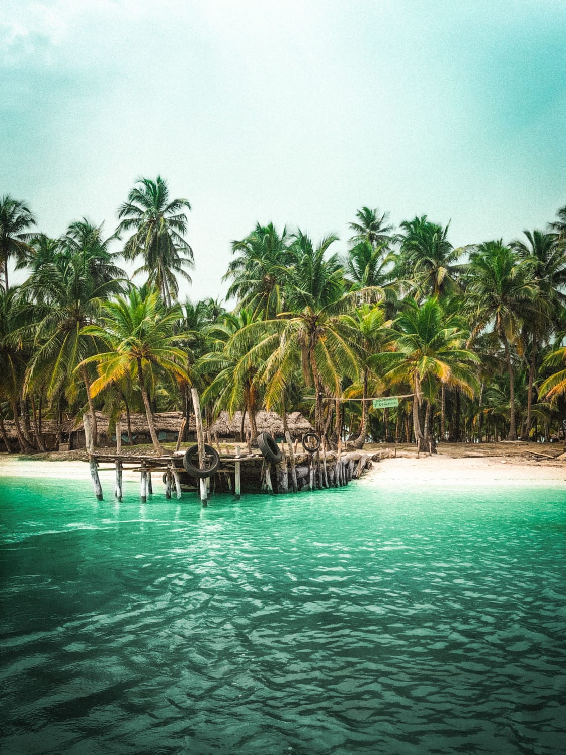 Une plage tropicale bordée de palmiers, avec un ponton en bois et une eau turquoise