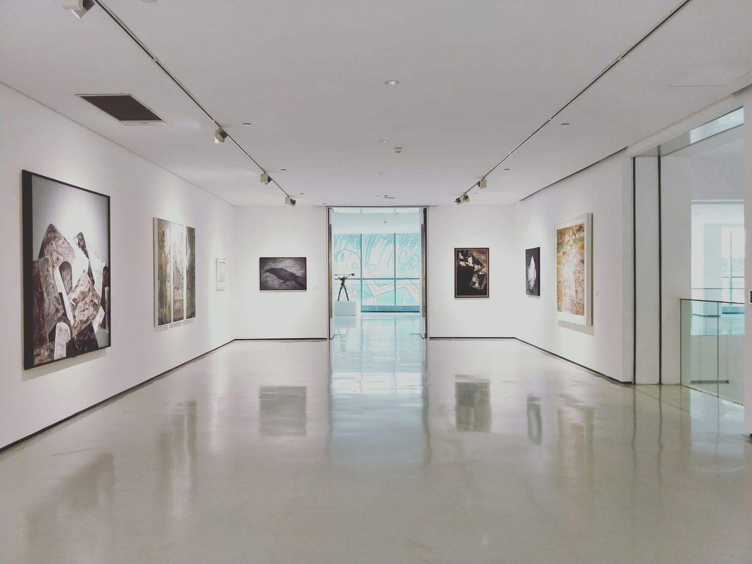Museum or gallery with art on both sides of white walls with a lot of glass windows in the distance.
