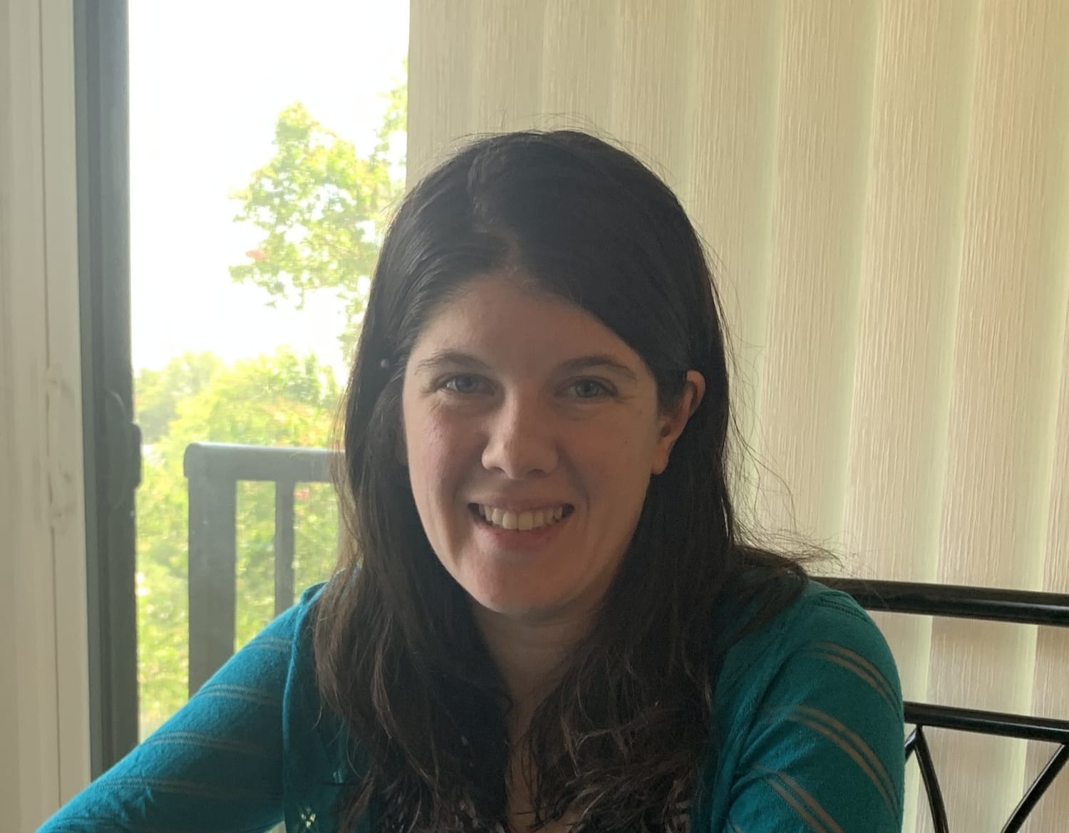Founder. Brunette with a teal sweater sitting on a chair.
