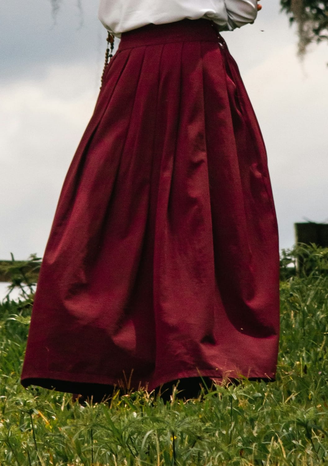 Cranberry petticoat with white blouse and green grass in the background. Photo by Guilherme Gomes Dos Santos on Unsplash.