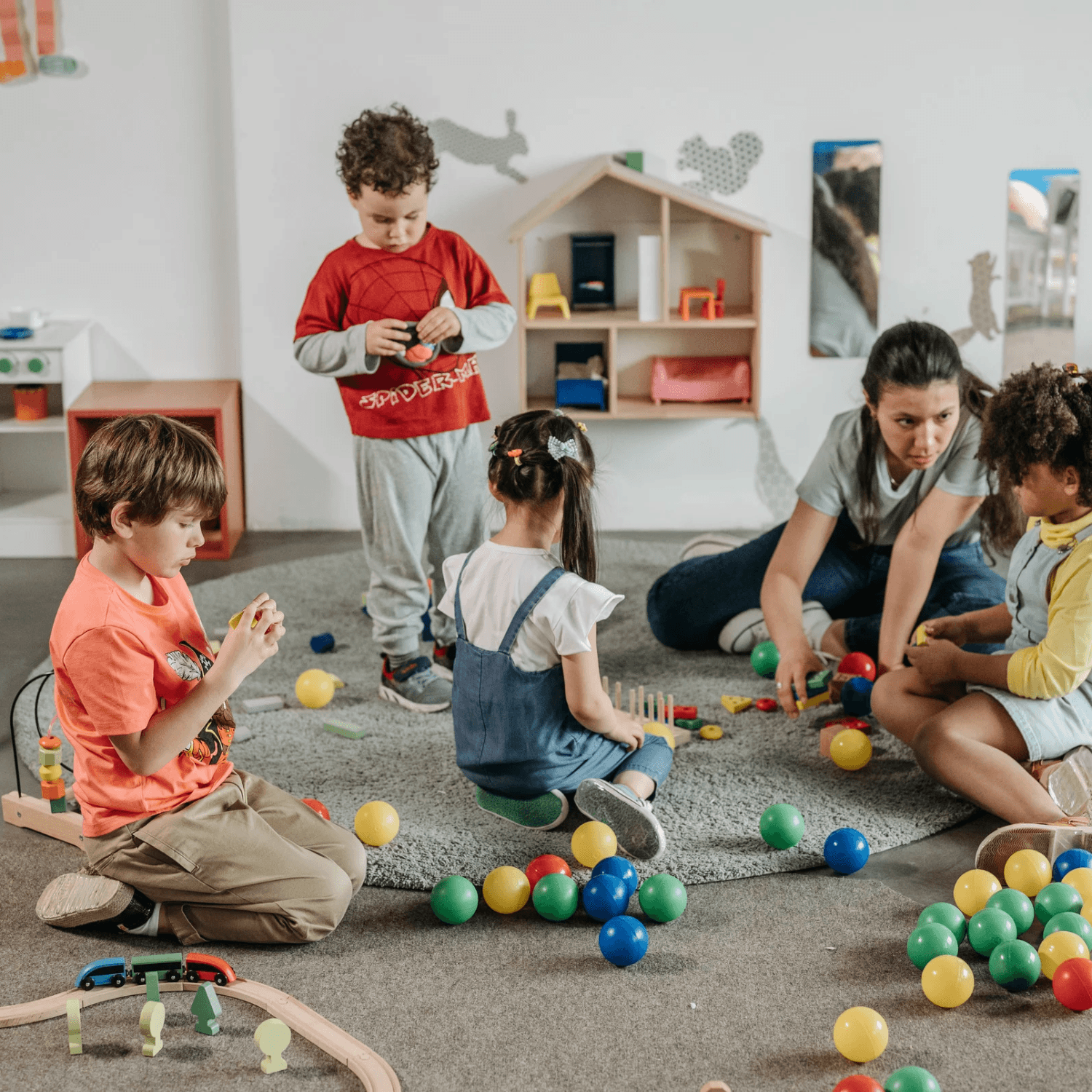 Group of children playing with blocks, a train set and small plastic balls. Educator is in the top right corner interacting with them.