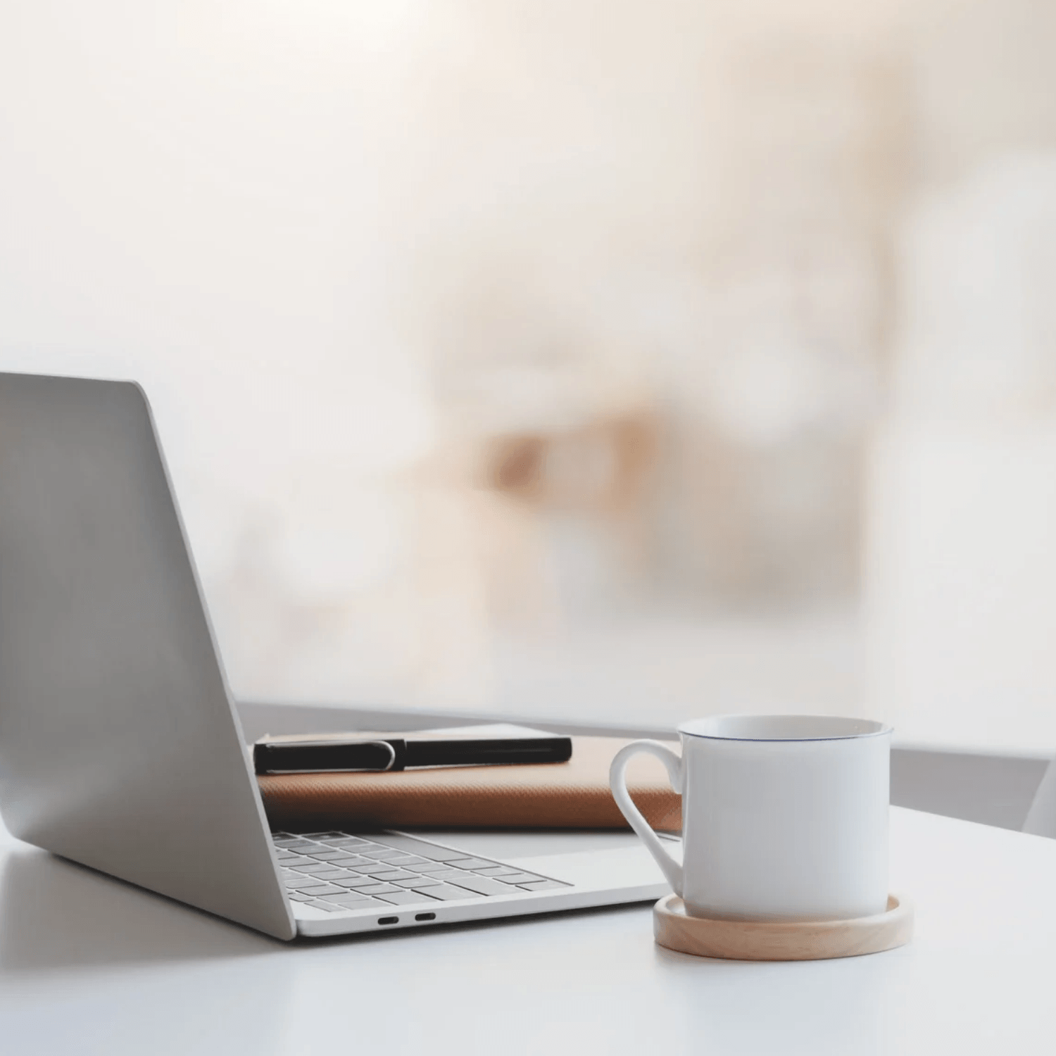 Silver laptop with a coffee mug to the side. A brown notebook and black fountain pen are in the back.