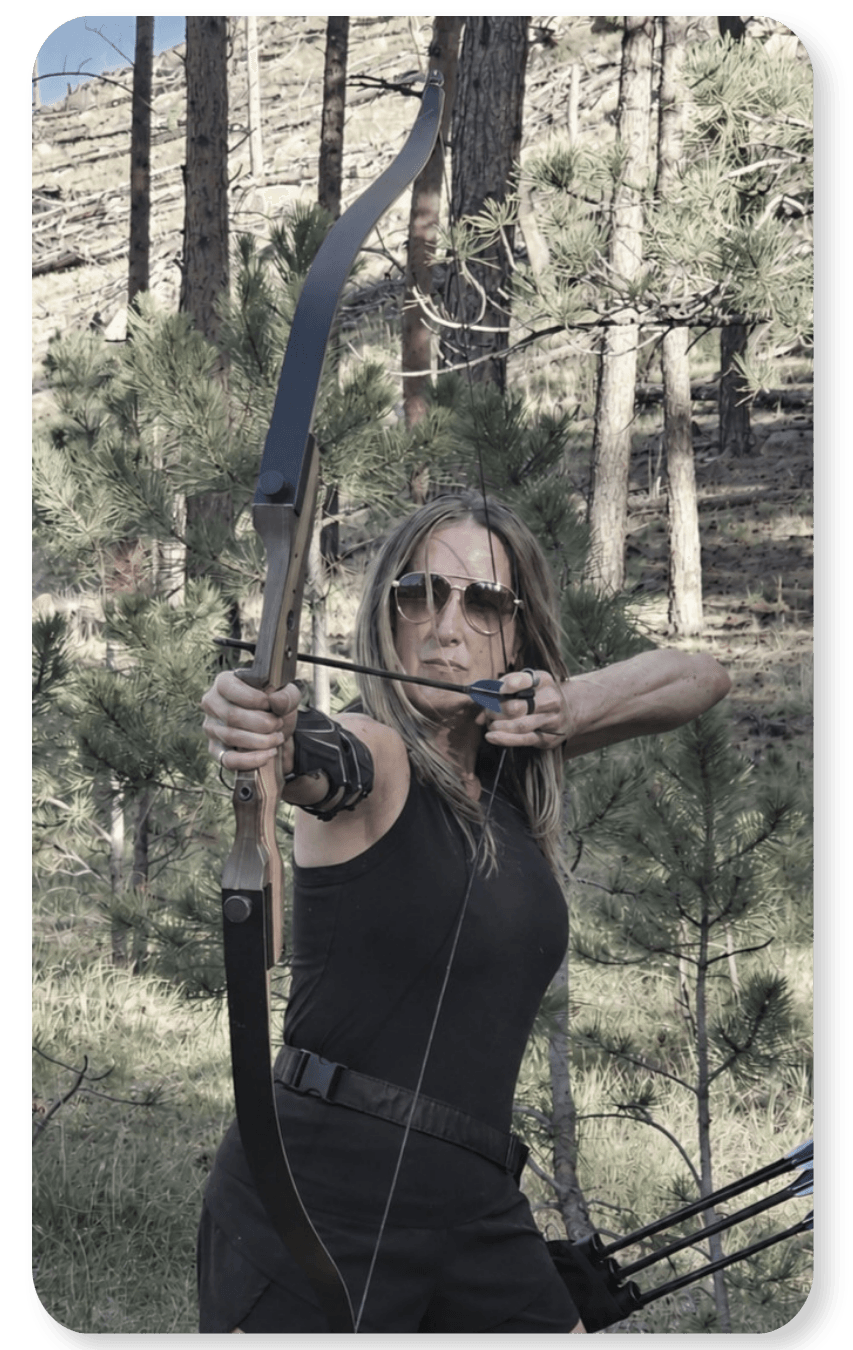 RoxAnne Eli aiming a bow and arrow outdoors