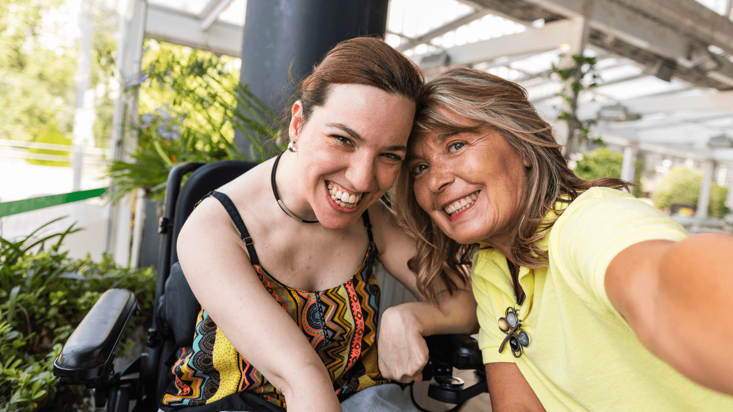 woman in a wheelchair and a woman holding a camera, both smiling