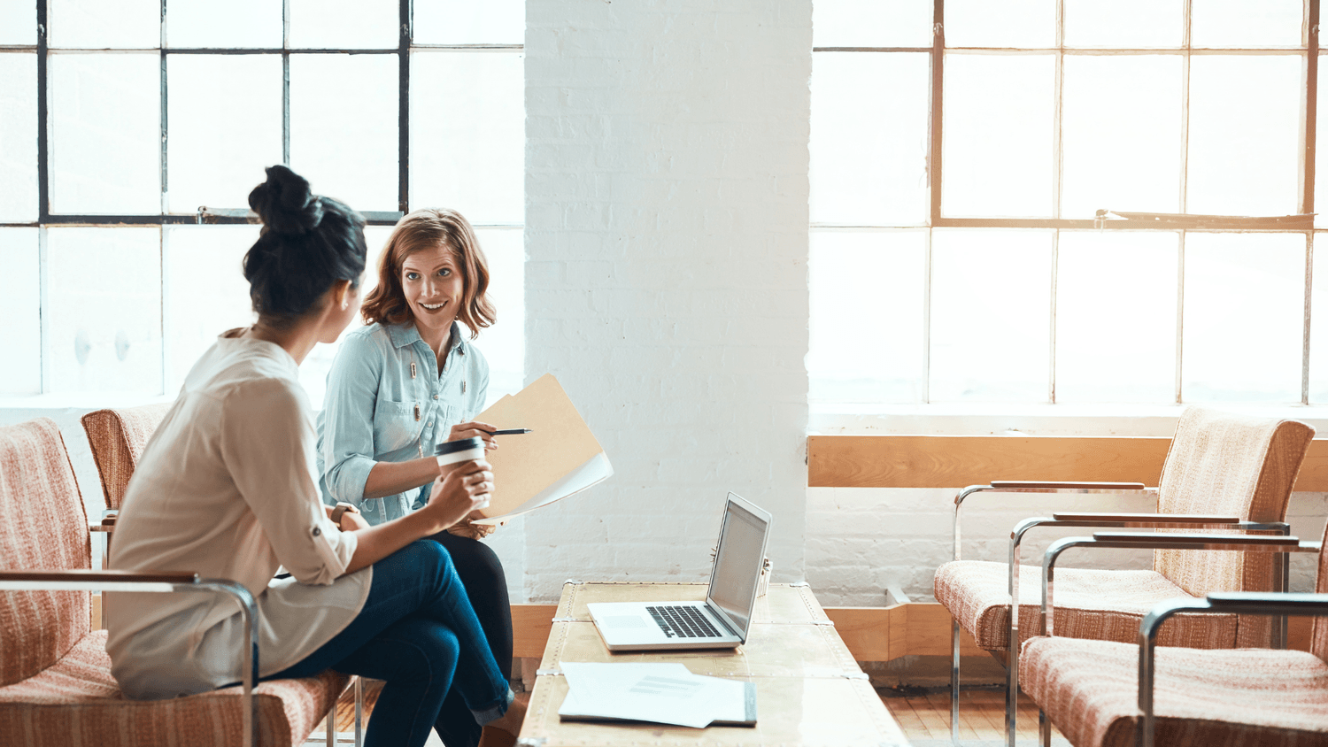 two women sat down talking in front of a laptop and paperwork