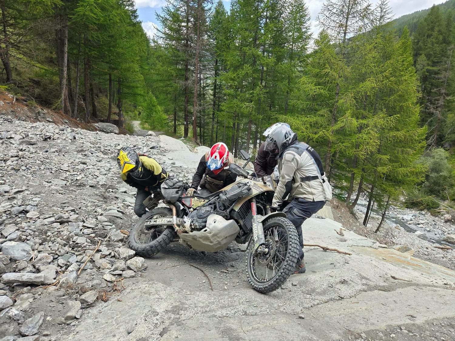 Motards qui relèvent ensemble une moto sur une piste de montagne