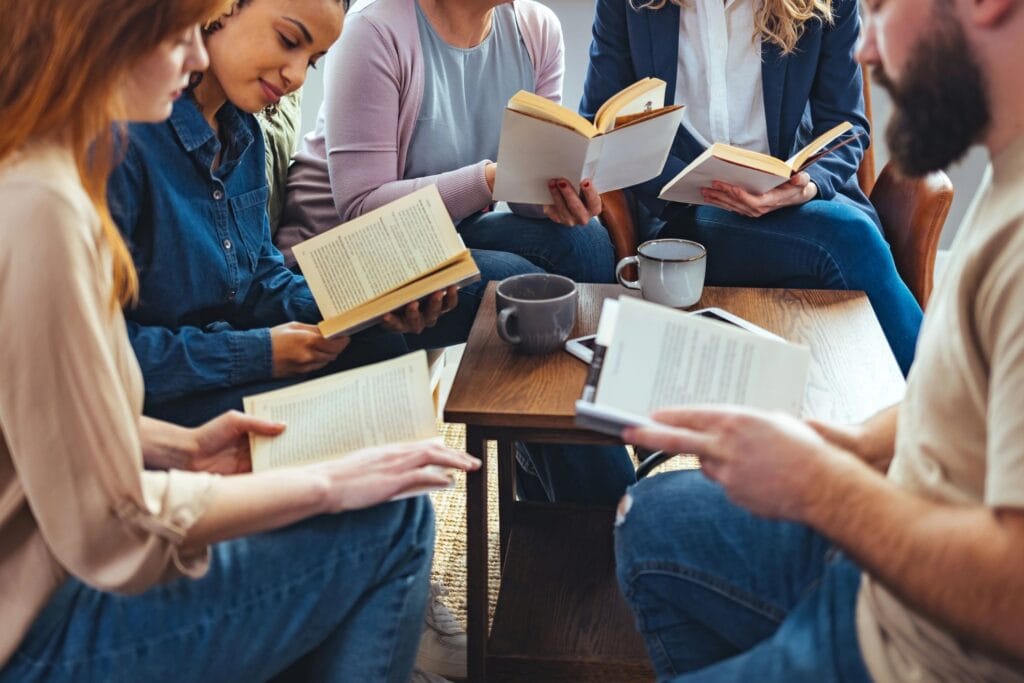 Un petit groupe de personnes d'âges variés, assises à une table, discutant et lisant des livres ensemble.