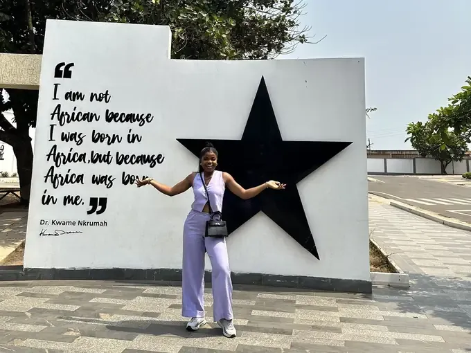 Geraldine in a lilac outfit in front of a black star monument