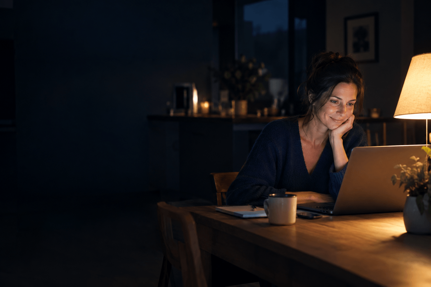 Une femme travaille sur son ordinateur, le soir, à la lumière d'une lampe