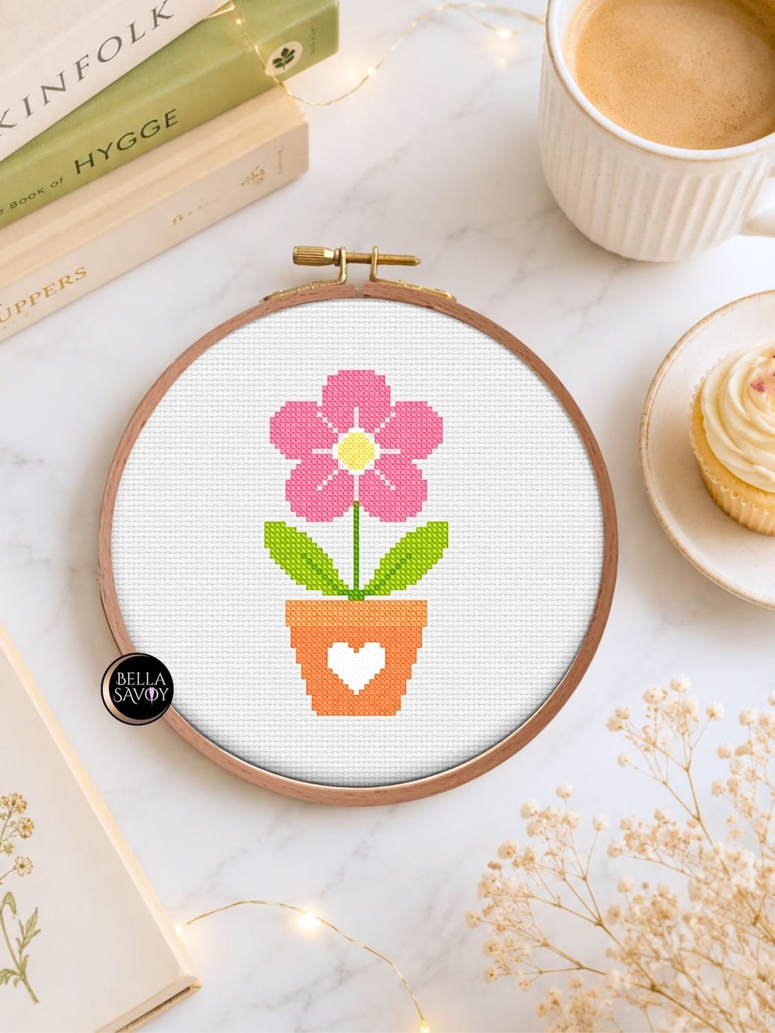 minimalist flatlay with a potted succulent embroidery on a hoop set against a white background with stag silhouette pattern. Surrounded by a cup of black coffee, a candle, and stem with leaves. Soft cast shadow