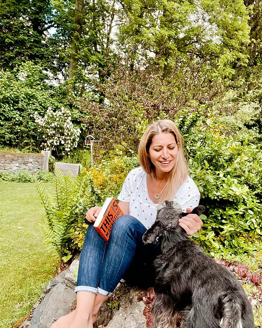 Kristin Voigt sitzt im Garten mit einem Buch und krault ihren Zwergschnauzer Pino