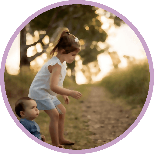 A girl leaping along a sunlit path while her little brother watches