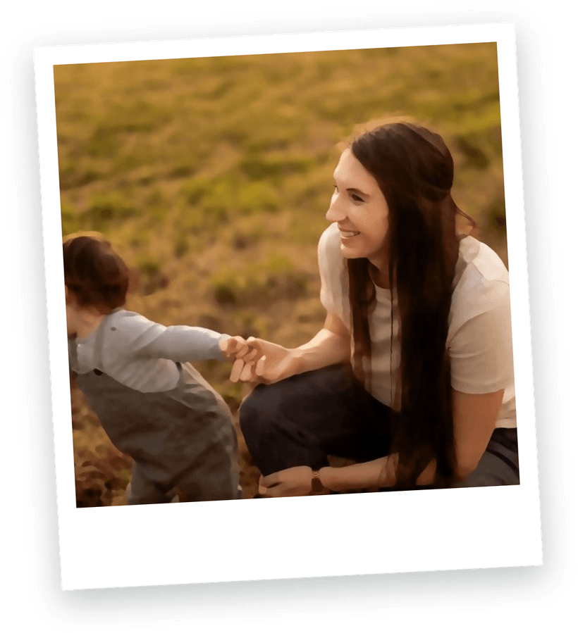 Jess kneeling in the grass, holding hands with her young son