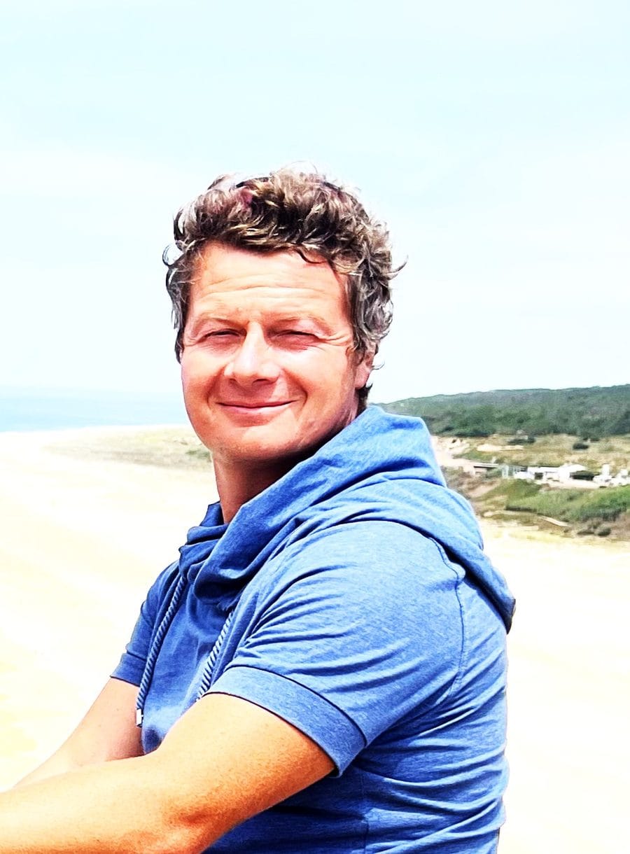 Marco lächelt, im Hintergrund Strand und Dünen