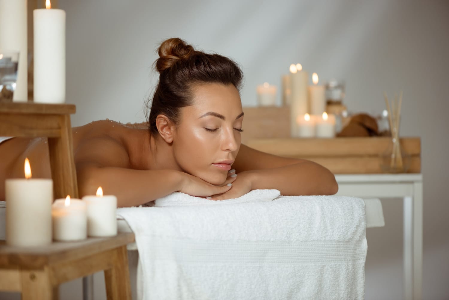 Femme allongée sur une table de massage, les yeux fermés, bougies
