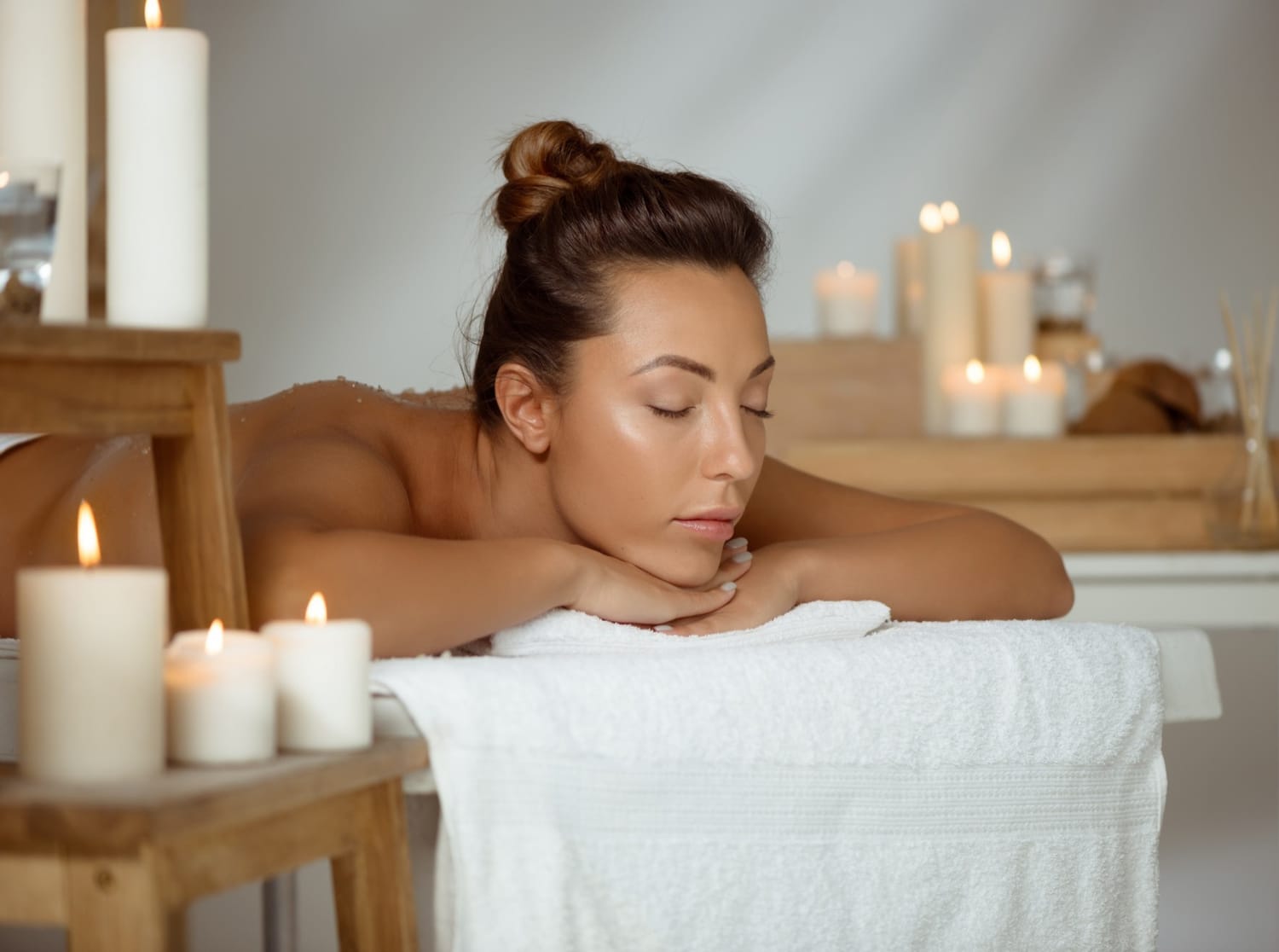 Femme allongée sur une table de massage, les yeux fermés, bougies