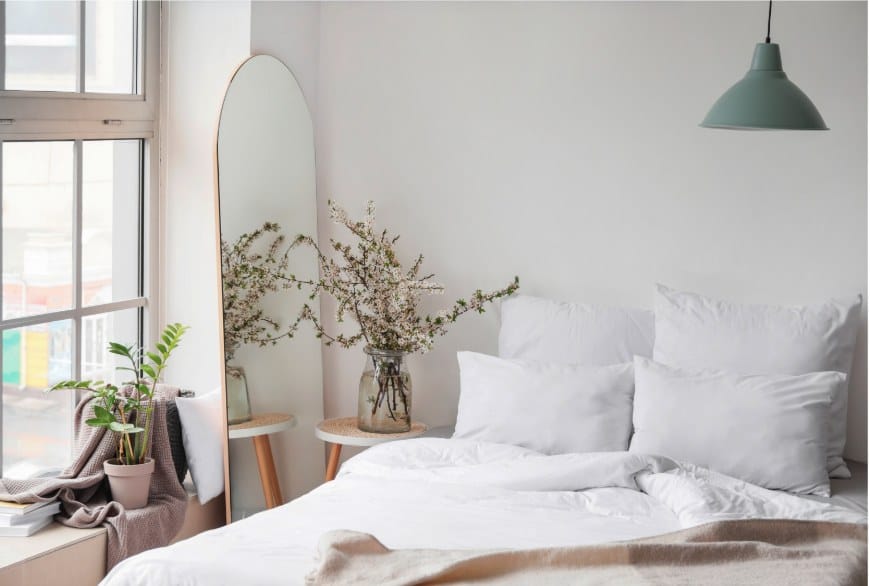 A light bedroom with a tall arched mirror and fresh blossom