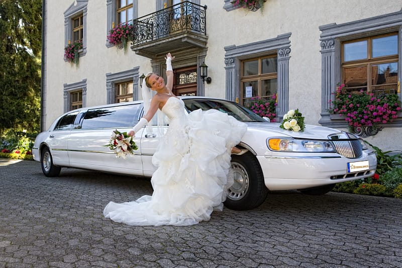 Braut posiert vor der weißen Hochzeitslimousine