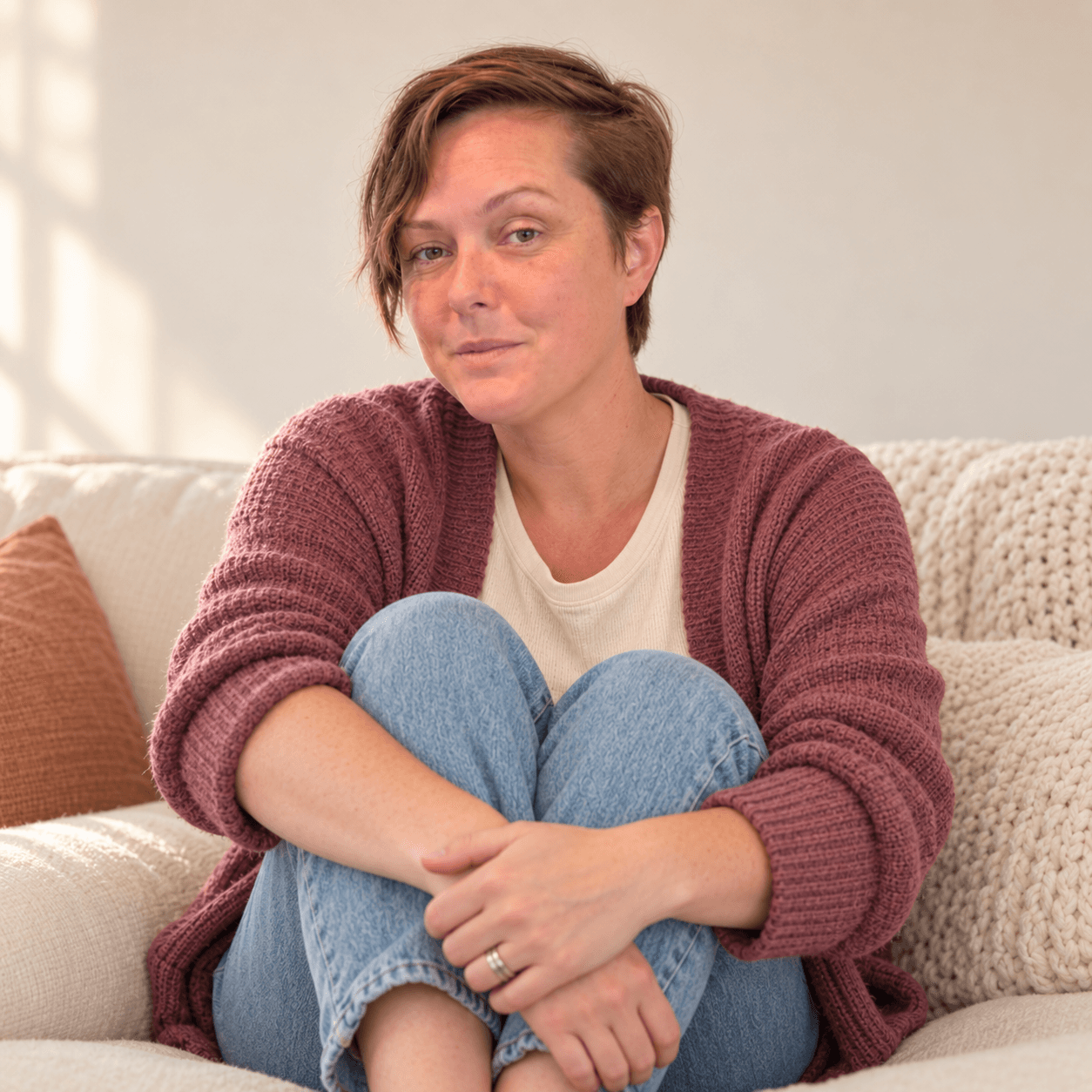 AI-edited portrait of Kelli seated comfortably on a cream sofa in a dusty rose cardigan