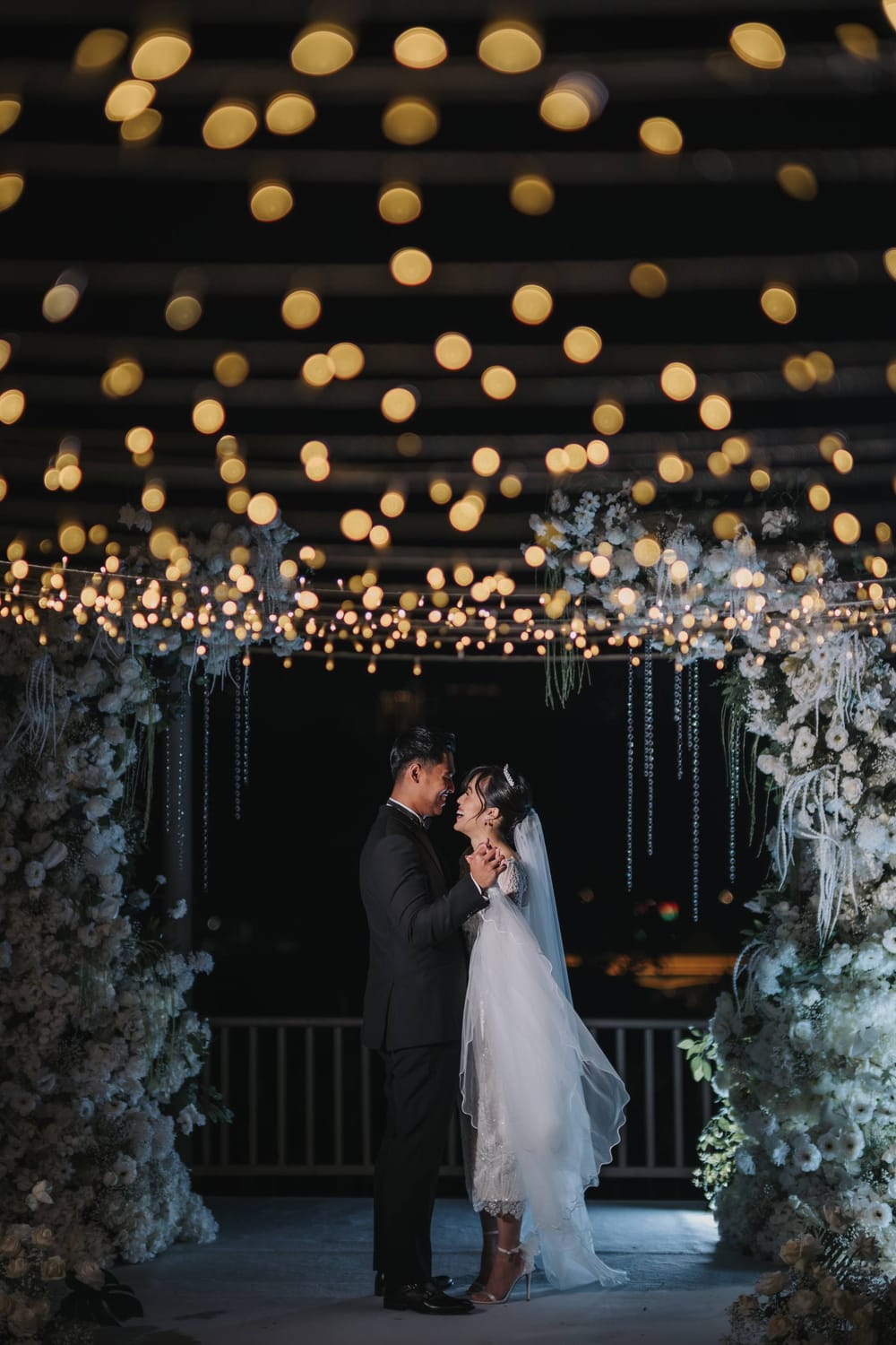 Bride and groom beneath a floral arch under evening lights