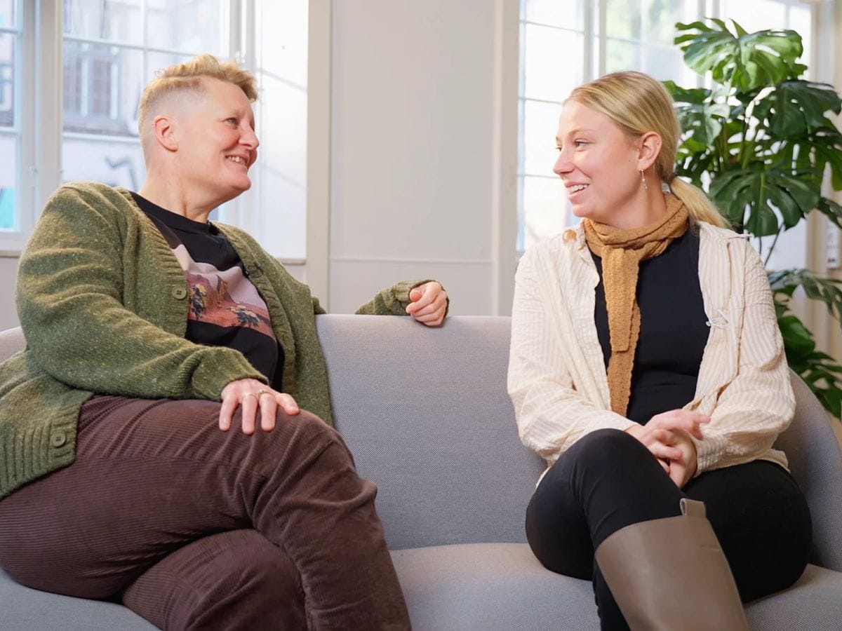 To medarbejdere fra Københavns Kommune smiler til hinanden i en sofa under optagelsen af en introvideo