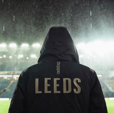 A supporter wearing a hooded jacket with LEEDS across the back at a rainy Elland Road.