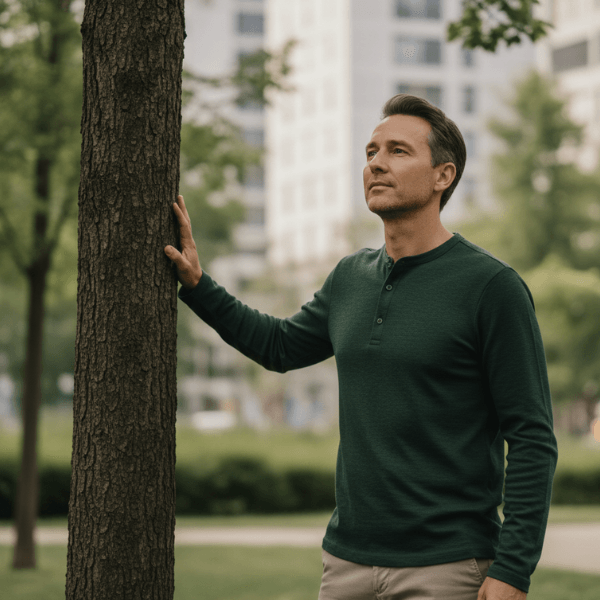 Homme en chemise verte posant la main sur le tronc d'un arbre dans un parc urbain
