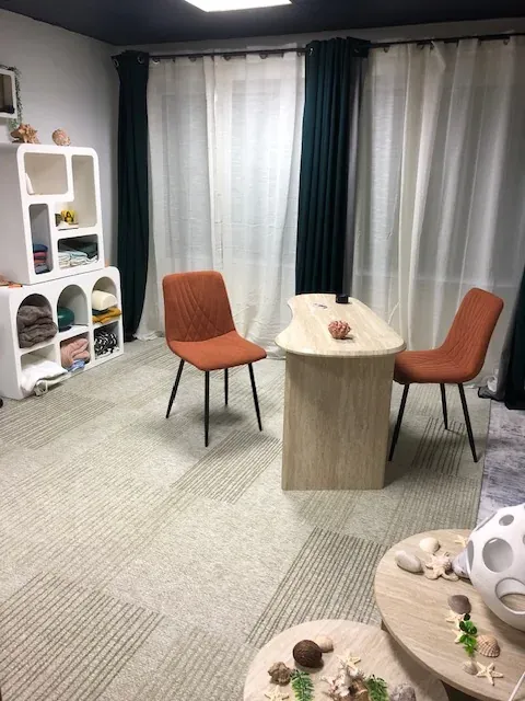 Le cabinet partenaire de Calais : deux fauteuils orange de part et d’autre d’une table en bois clair, devant des rideaux