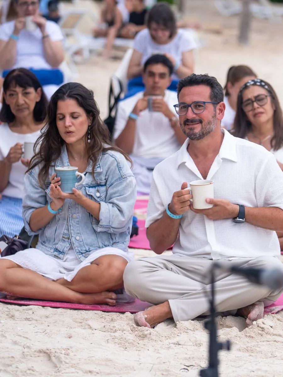 Tony Espigares sentado en la arena entre participantes, en la ceremonia de cacao de Cancún 2025