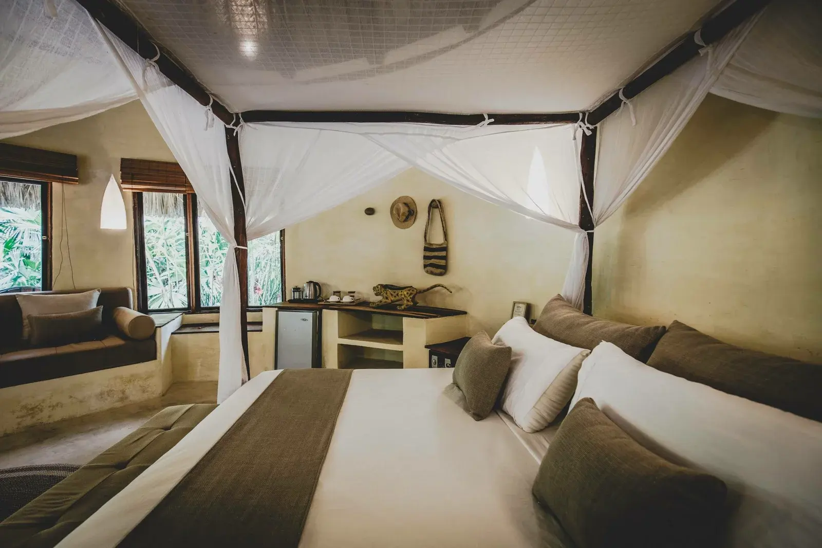 Cama con dosel blanco bajo el techo de palma de una cabaña