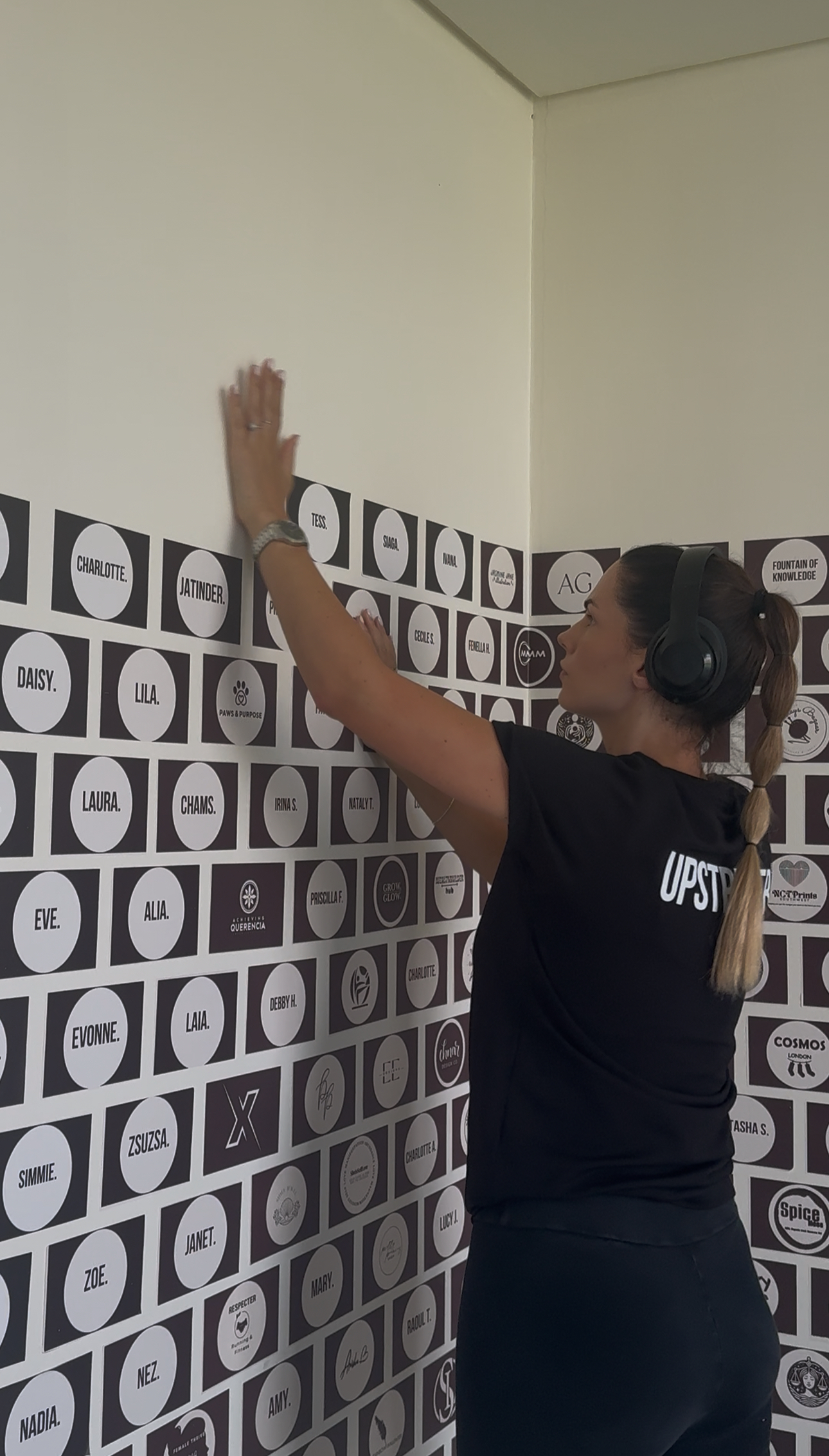 Anne adding a new member name to the Upstrider Wall, wearing headphones and a branded Upstrider shirt – showcasing dedication, community, and personal mentorship for each client’s success journey.