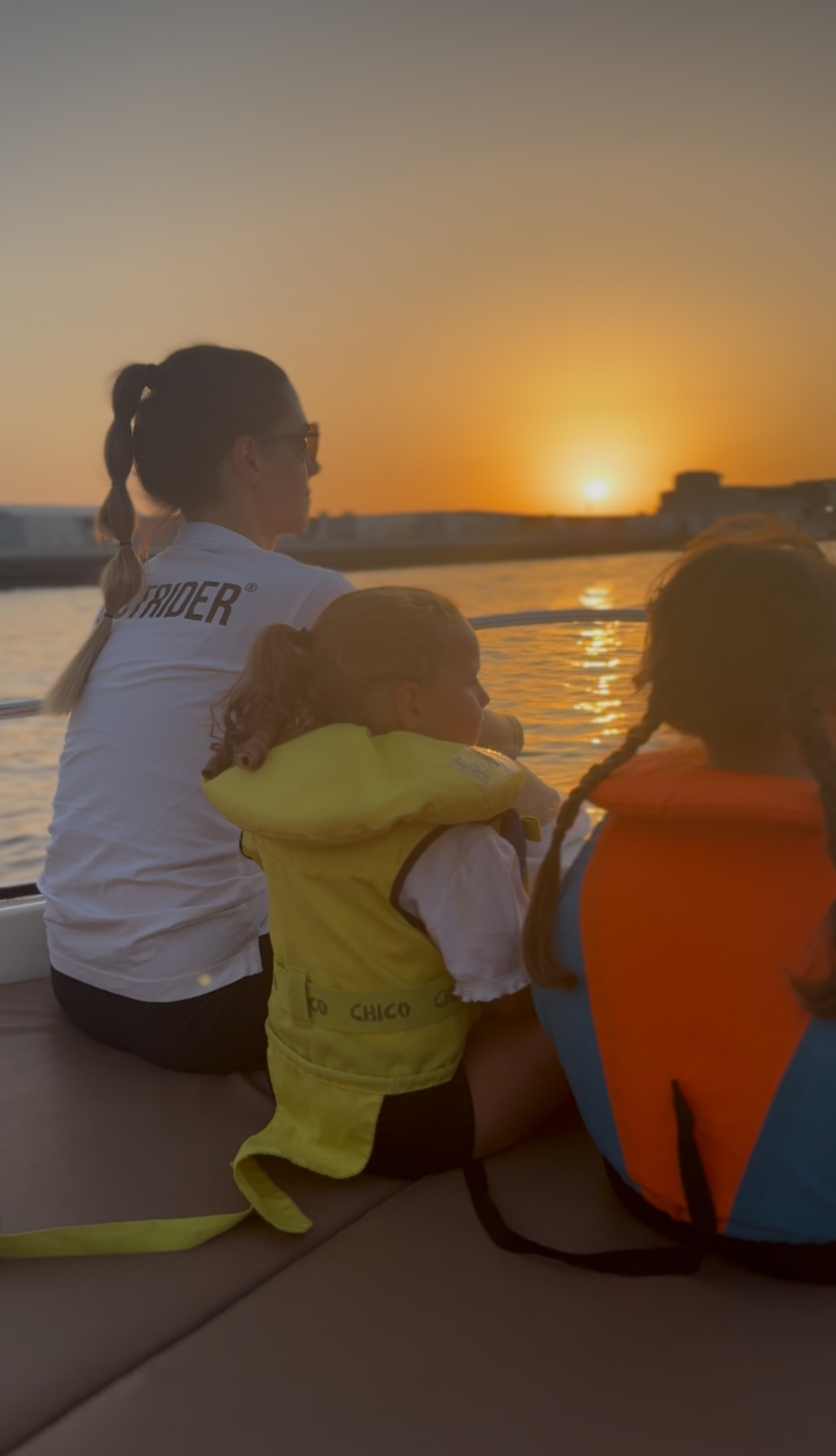 nne and her two daughters watching the sunset from a boat in Dubai, wearing life vests and Upstrider t-shirt – symbolising family, freedom, and the power of building a life by design