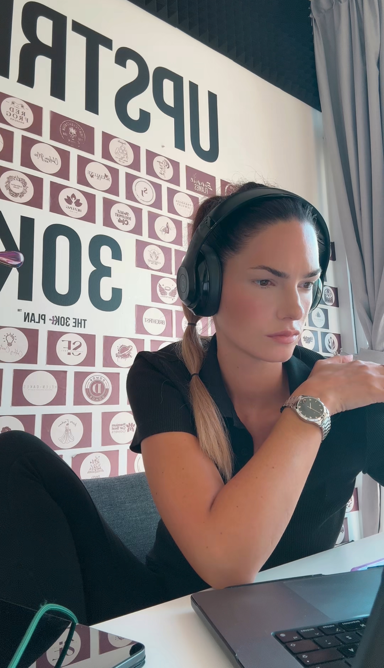 Anne from Upstrider working with focus at her desk in front of the 30K+ Plan™ success wall, wearing headphones.