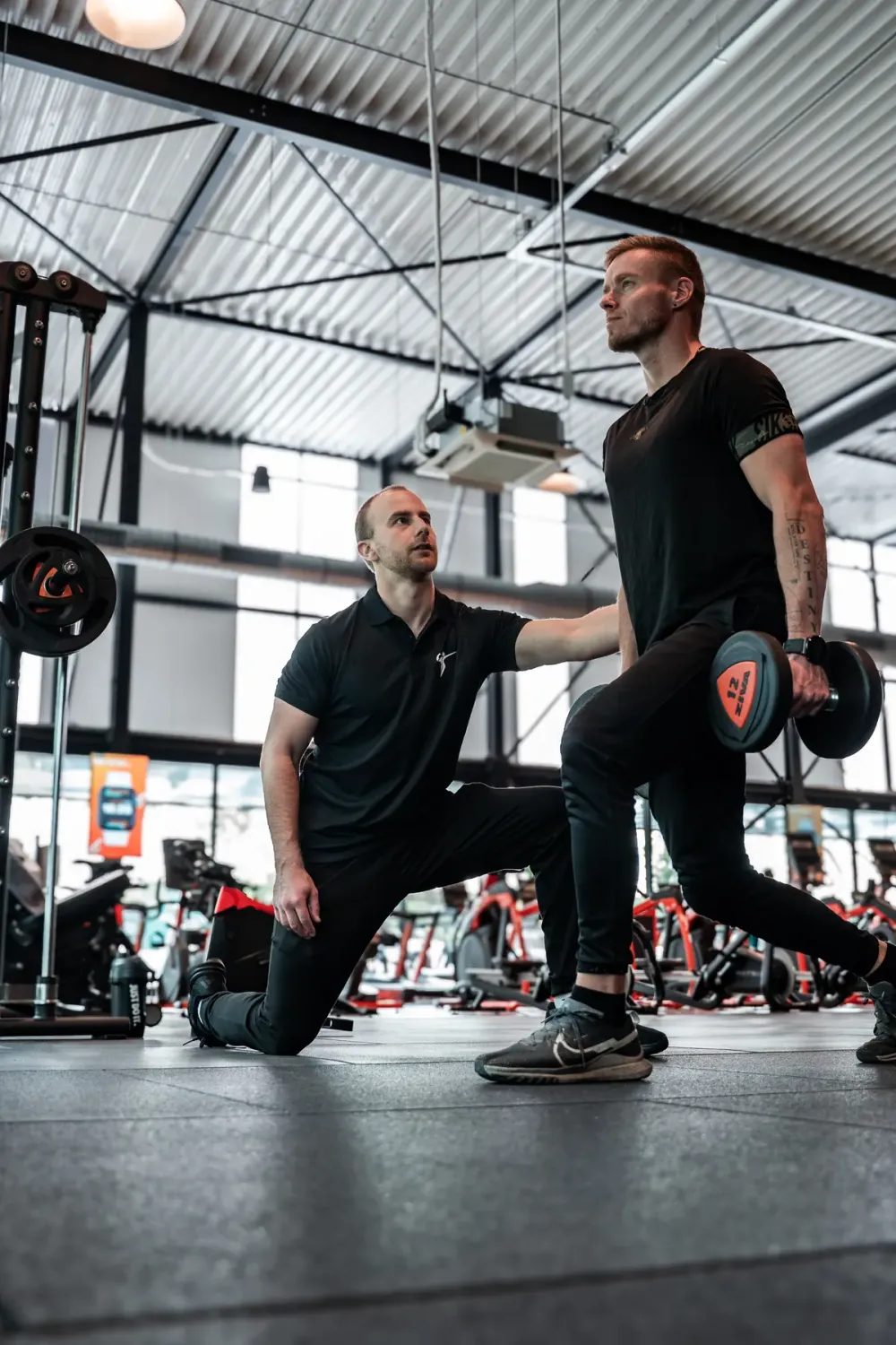 Personal trainer van 2Refocus coacht een lunge met dumbbells in de Basic-Fit