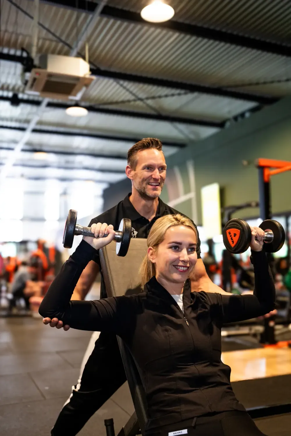 Personal trainer van 2Refocus begeleidt een klant bij de schouderpers met dumbbells