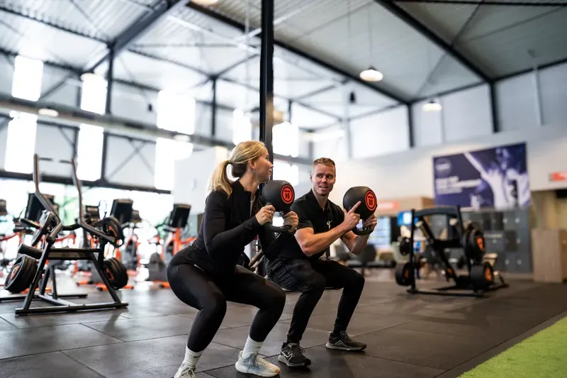 Trainer en klant doen samen een squat met kettlebells