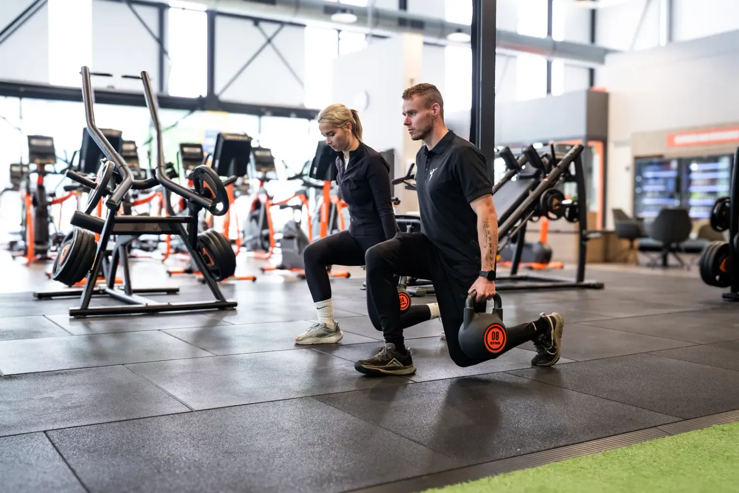 Trainer doet een lunge met kettlebell voor aan een klant