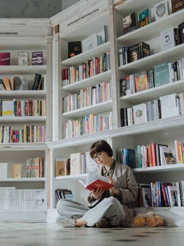 Woman in Grey Suit Sitting on Floor Beside Book Shelf