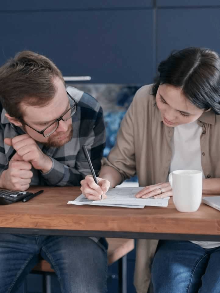 Woman in Brown Shirt Writing on Paper Beside a Man