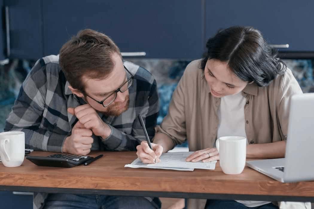 Woman in Brown Shirt Writing on Paper Beside a Man
