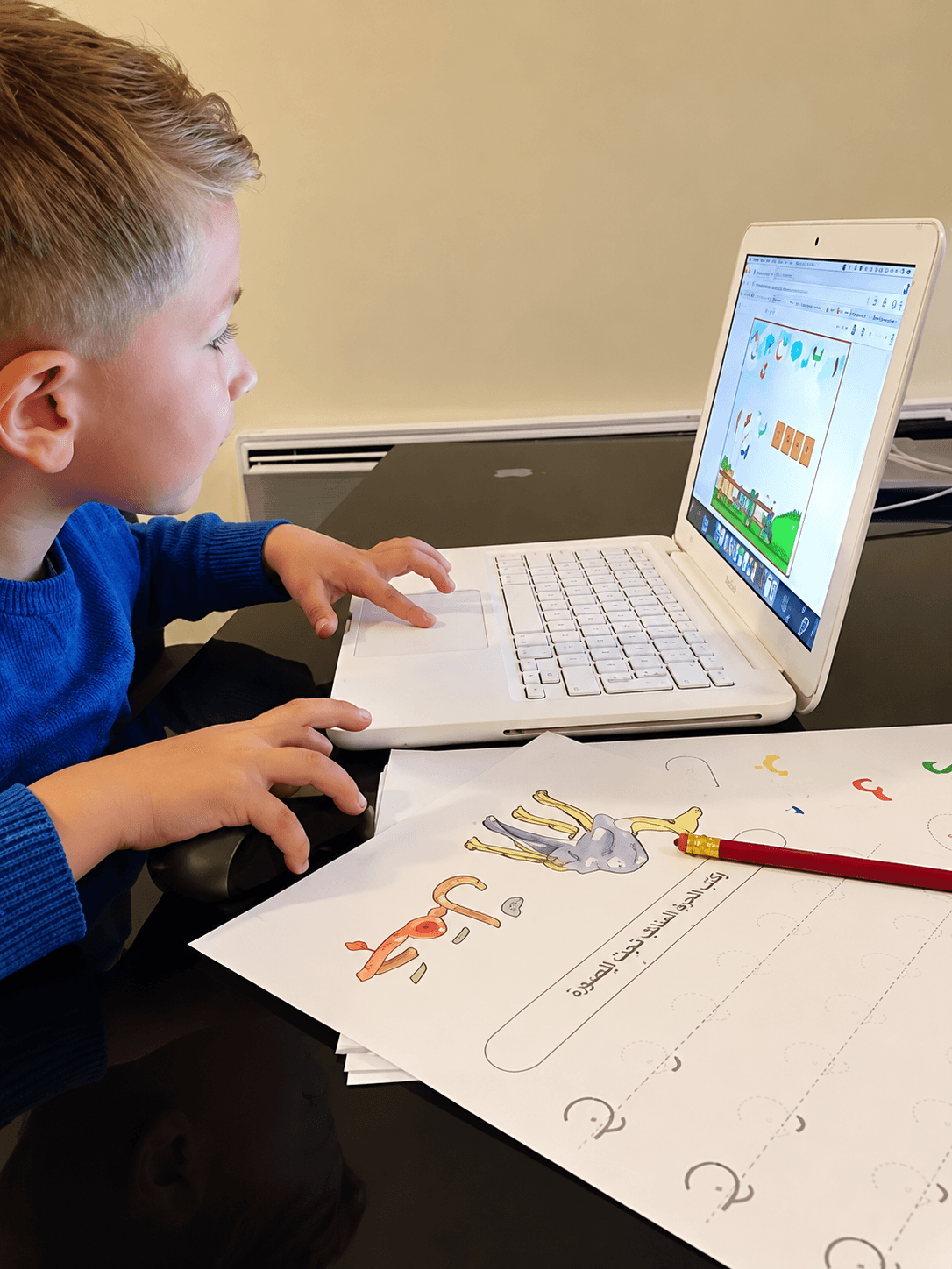 Un petit garçon suit le programme sur l'ordinateur avec les activités à imprimer