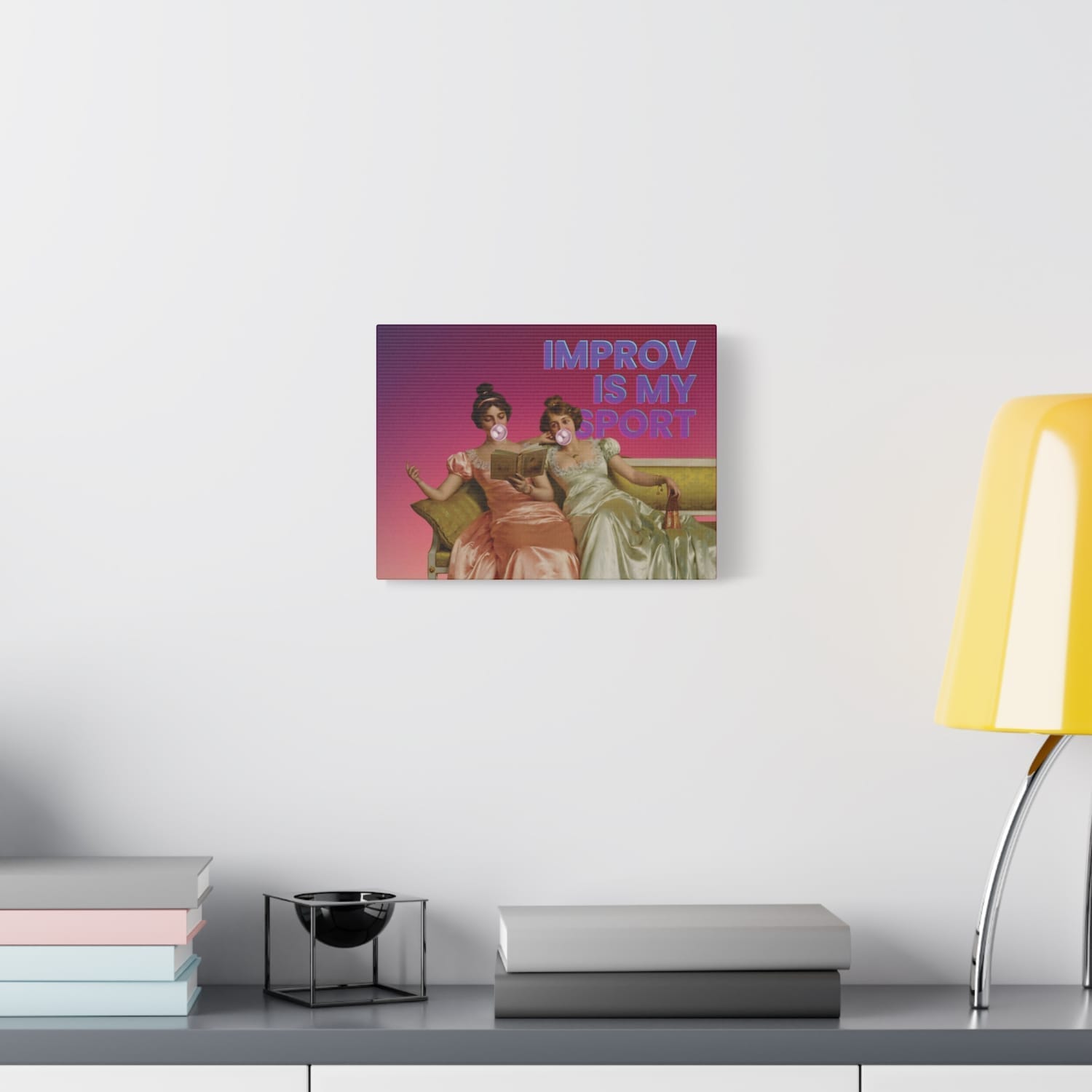 hanging on the wall above a desk with a yellow shaded lamp A whimsical canvas print featuring Victorian ladies lounging on a couch, one blowing a bubble gum bubble, with the text "Improv Is My Sport" celebrating creativity and spontaneity.