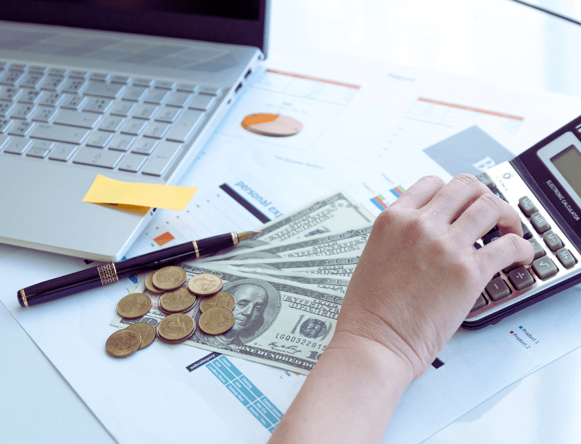 Femeie organizându-și bugetul personal: bancnote, monede și calculator financiar alături de laptop, într-un moment de reflecție asupra banilor, parte dintr-un ritual financiar regulat.