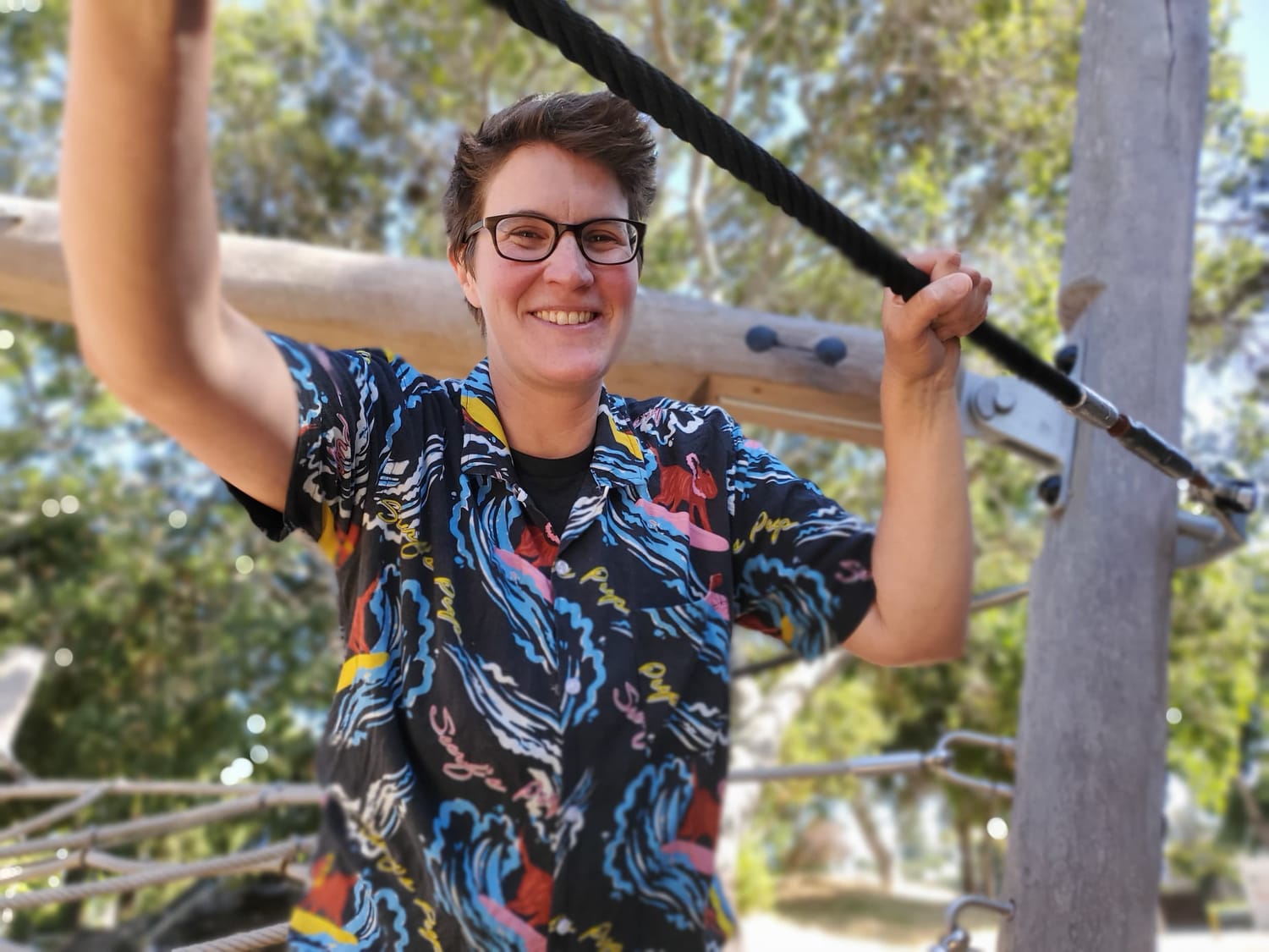 Rose Slam Johnson, founder of Nimble Roots Coaching and small business coach for The Queer MBA, smiling warmly outdoors in a bright fun patterned shirt.