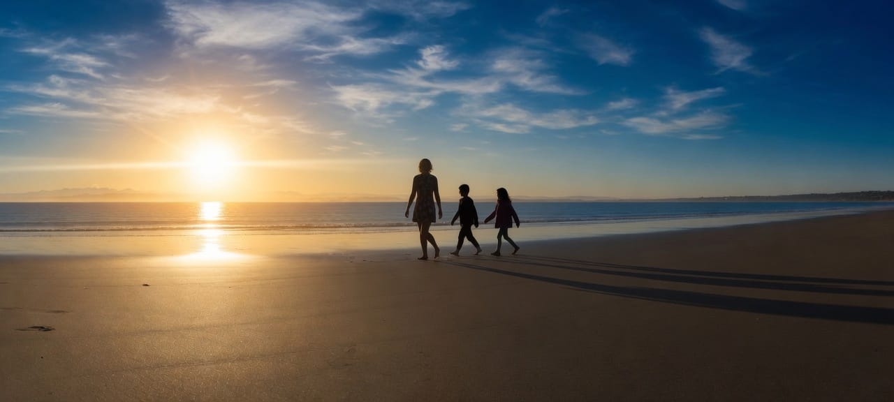 A woman and two children walking the beach at sunrise.