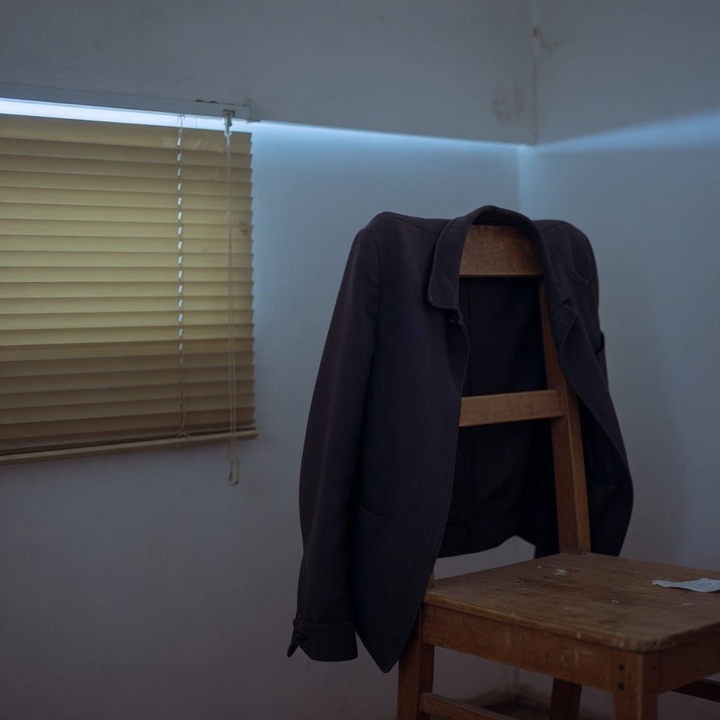 A work jacket on a chair beside closed blinds.