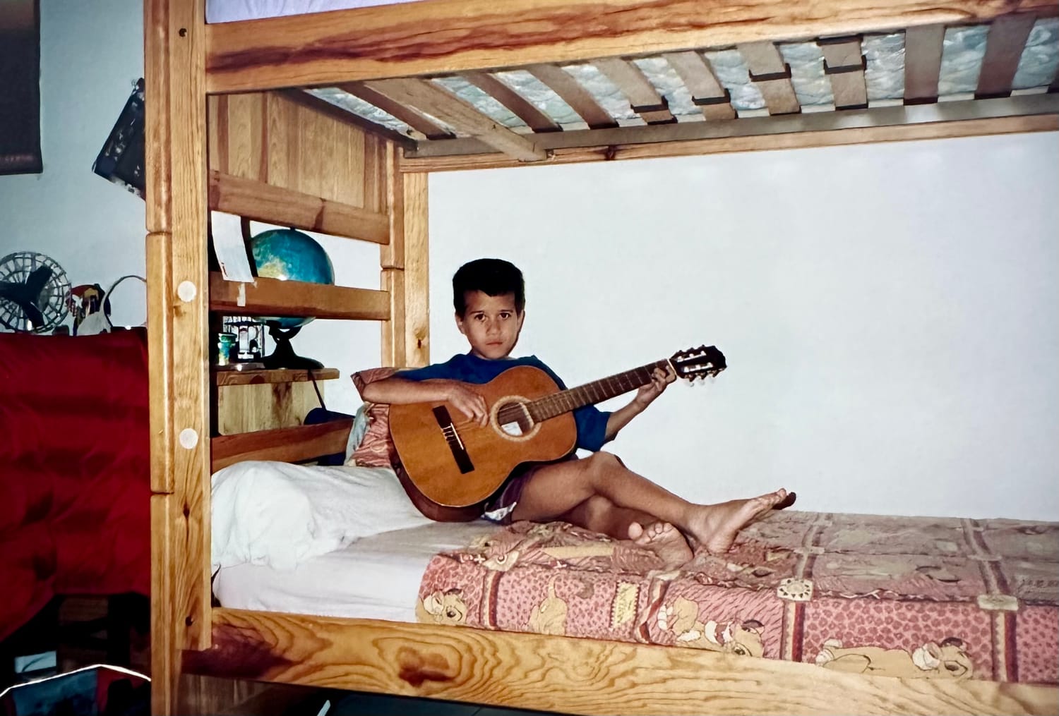 Christophe enfant avec sa guitare sur un lit
